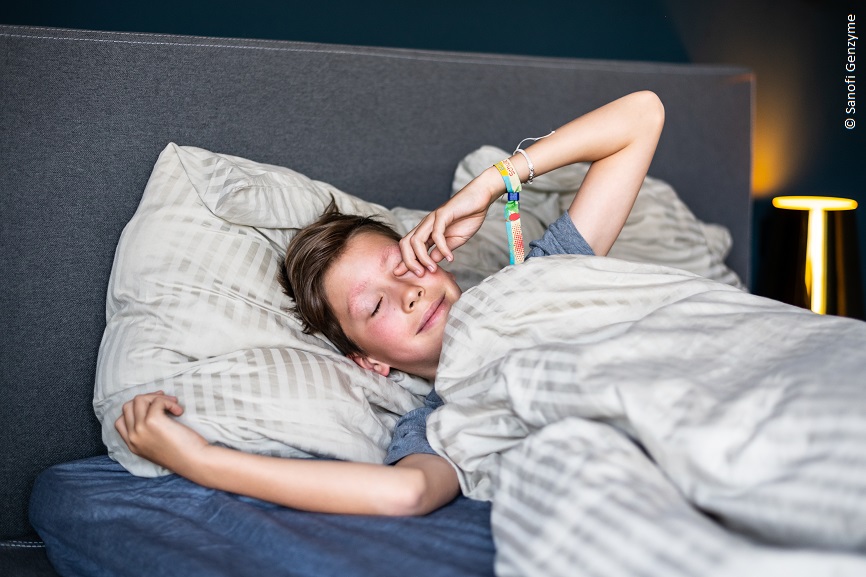Eine Junge liegt im Bett und reibt sich die Augen. 